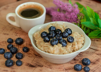 Oatmeal with blueberries for breakfast with coffee on a wooden table. Traditional healthy breakfast. Oatmeal and espresso. Close-up