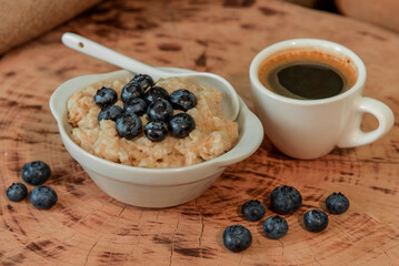 Oatmeal with blueberries for breakfast with coffee on a wooden table. Traditional healthy breakfast. Oatmeal and espresso. Close-up