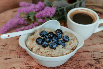 Oatmeal with blueberries for breakfast with coffee on a wooden table. Traditional healthy breakfast. Oatmeal and espresso. Close-up