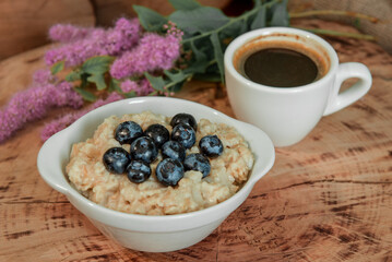 Oatmeal with blueberries for breakfast with coffee on a wooden table. Traditional healthy breakfast. Oatmeal and espresso. Close-up