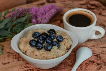 Oatmeal with blueberries for breakfast with coffee on a wooden table. Traditional healthy breakfast. Oatmeal and espresso. Close-up