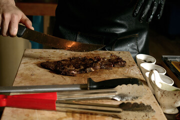 Chef cuts a grilled meat on a wooden Board, close-up