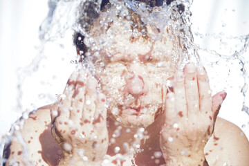 The guy washes his face with water, drops fly in different directions, on a white background