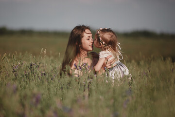 Happy family: a young beautiful pregnant woman with her little cute daughter walking in the wheat field on a sunny summer day. Parents and kids relationship. Nature in the country.