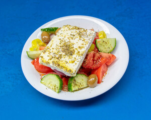 Fototapeta na wymiar fresh Greek salad plate on vibrant blue table background