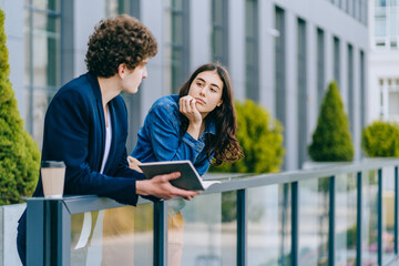 Portrait of charming woman looking aside and hesitating while man trying to kiss her cheek isolated over yellow background