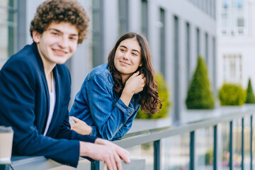 Image of kind students couple man and woman waving by hand, smiling at urban background outdoors. Concept Education lifestyle. Close up portrait.