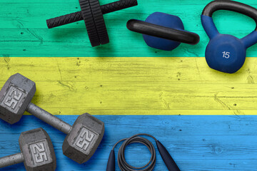 Gabon sports club concept. Top view of heavy weight plates with iron bar on national background.