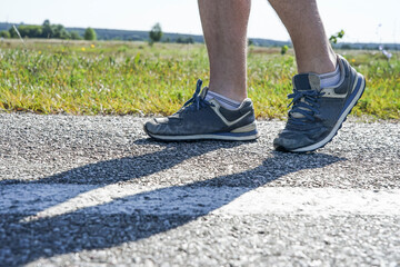 man runs on an asphalt road, legs in sneakers close-up
