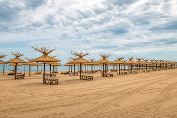 Beauty wooden umbrellas and sunbeds in a row of empty sandy beach