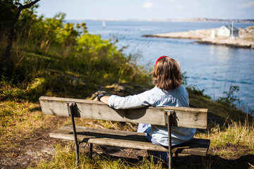 A young woman sitting on a bench enjoying a view over the Swedish west coast, Sweden