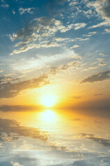 Sunset over a calm sea with bright sunrays and clouds.