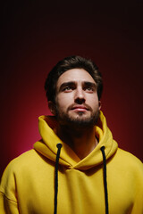 Portrait of a young guy 25-30 years old looking up in a yellow sweatshirt on red wall background. 