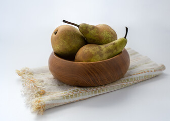 Three pears in a wooden bowl on a tea towel.  Natural light and vintage look.