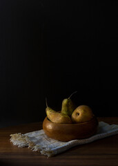 Still life with pears in a wooden bowl on a black background.
