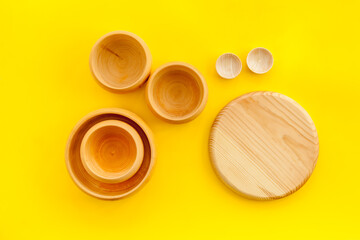 Set of rustic wooden tableware - bowls and utensils on yellow background top view