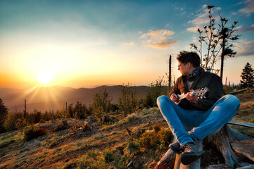 Ein Junge spielt einen Instrument und schaut dem Sonnenuntergang entgegen