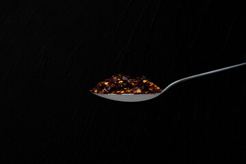 Isolated spoon full of  chilli pepper in a black background