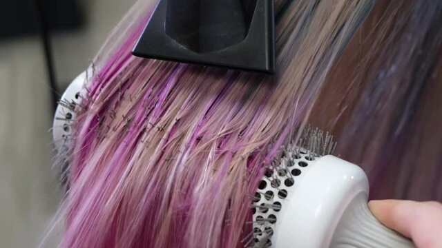 The hairdresser dries the blond hair of the client after dyeing it blue and red.