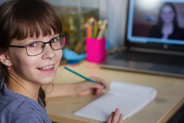Fotobehang Online onderwijs op afstand. Een gelukkig meisje studeert thuis en maakt huiswerk op school. © Albert Ziganshin
