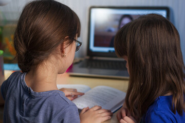 Two girls reading a book. A home distance learning