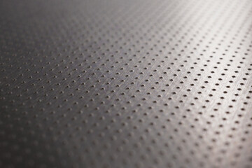 Industrial dark gray metal background or wallpaper. Perforated aluminum surface with many holes. Their ranks go into the distance and form a perspective. Abstract technological backdrop. Macro