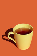 hot tea in a yellow plastic cup against orange background. hard light and deep shadows picture with space for text 