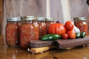fresh tomatoes and jalapenos from a family farm vegetable garden with garlic and red onion for home canned spicy salsa in glass jars on a rustic background