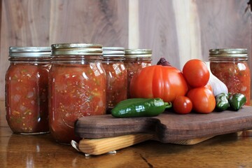 fresh tomatoes and jalapenos from a family farm vegetable garden with garlic and red onion for home canned spicy salsa in glass jars on a rustic background - obrazy, fototapety, plakaty