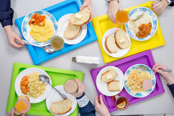 Children are having lunch in the school cafeteria. Top view of dishes on colored trays.