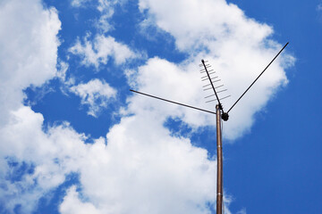 Obraz premium External television antenna on a background of bright blue sky and cotton clouds. Shot in the summer in the country. Vivid illustration on the topic of media, TV news and digital broadcasting