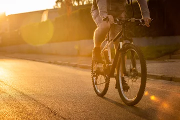 Rolgordijnen Man riding a bicycle with a sunset background. © Pratiwi
