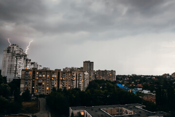 Landscape view on buildings in Kyiv with thunder above the house. Rainy weather with storm in the city in day time. City skyline with bad weather and twilight day with lights in the windows. 
