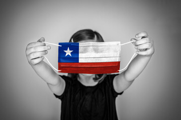 A child girl show a protective medical mask against bacteria and viruses with the flag of Chile.