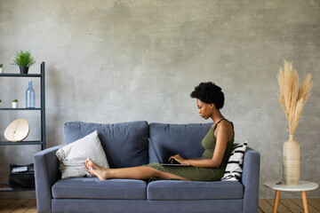 Happy african American young woman sit relax on cozy couch and working on a laptop. Happy to move...