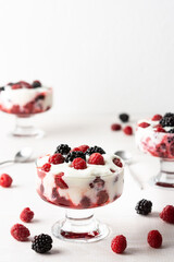 Delicious juicy berries of raspberries and blackberries with yoghurt in a glass form on a white background