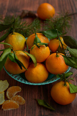 Closeup basket with ripe juicy tangerines and coniferous twigs on a brown wooden table