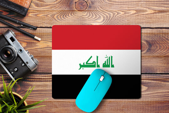 Iraq flag on wooden background with blue wireless mouse on a mouse pad, top view. Digital media concept. - Powered by Adobe