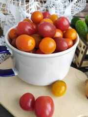 Food still life red and yellow cherry tomatoes in a ceramic bowl on a wooden table with a lace napkin