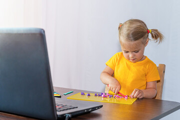 Naklejka premium A child makes plasticine at home, watching a lesson on the Internet. Online education.