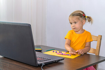 An interested little girl looks at her laptop and sculpts out of plasticine.