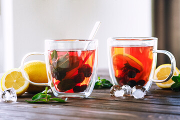 two glass cups of iced berry tea with lemon slices and mint