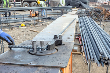 The worker is bending rebars (rods) in the construction site.