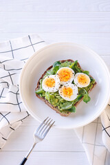 Hard boiled egg on avocado toast with freen leaves, healthy breakfast or lunsh, top view