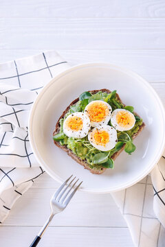 Hard boiled egg on avocado toast with freen leaves, healthy breakfast or lunsh, top view