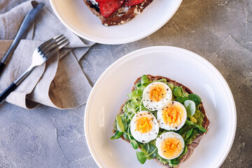 Hard boiled egg on avocado toast with green leaves and toast with fresh strawberries and cream cheese, healthy breakfast or lunsh, top view