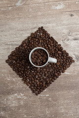 top view of a cup with coffee beans with a square figure in the background