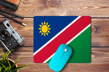 Namibia flag on wooden background with blue wireless mouse on a mouse pad, top view. Digital media concept.