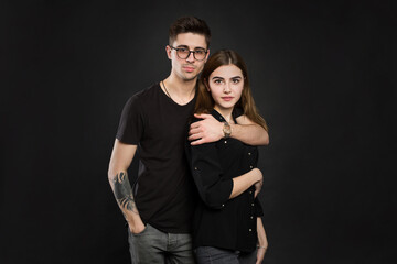 Portrait of young couple in black clothes wearing trendy glasses and posing over black background.