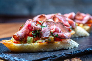 Bruschetta with ham or roast beef is on a slate plate.